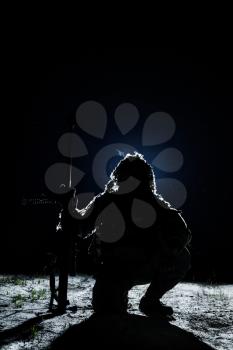 Army sniper with big rifle sitting holding rifle on black background. Lone killer in the moonlight