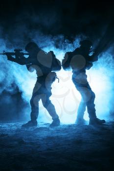 Pair of army soldiers attacking in the smoke. Backlit silhouette, toned image. Army storm concept
