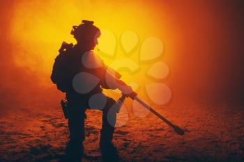 Army sniper with large caliber rifle sitting in the fire and smoke. Backlit silhouette, toned image