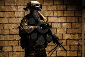 US Army Ranger with machinegun and night vision goggles standing near the wall. Side view profile