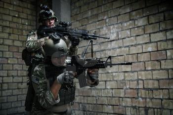 Pair of US Army Rangers with machinegun and rifle moving along the wall after each other on military mission
