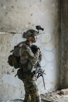 US Army Ranger with machinegun and night vision goggles standing near the wall. Side view profile