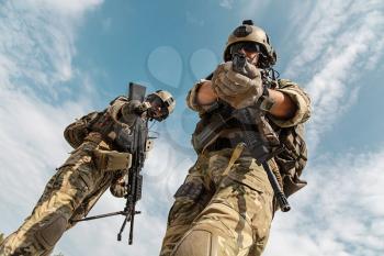 US Army Rangers pointing weapons to the camera detaining person. Low angle view