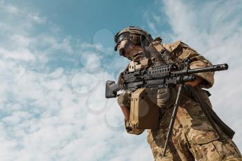 Low angle portrait of US Army Ranger with machinegun on blue sky background looking up. National pride concept