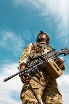 Low angle portrait of US Army Ranger with machinegun on blue sky background looking up. National pride concept