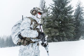 Winter arctic mountains warfare. Action in cold conditions. Trooper with weapons in forest somewhere above the Arctic Circle. Profile, side view