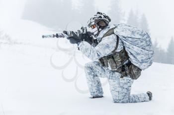 Winter arctic mountains warfare. Action in cold conditions. Trooper with weapons in forest somewhere above the Arctic Circle on the knee