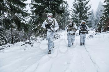 Winter arctic mountains warfare. Action in cold conditions. Squad of soldiers with weapons in forest somewhere above the Arctic Circle