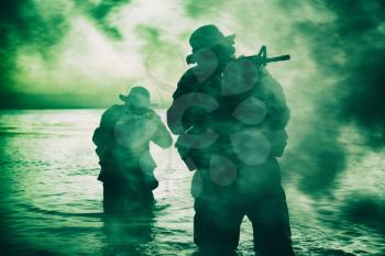 Commando soldiers walking in water, army special operations forces fighters sneaking in darkness, aiming assault rifles and observing shore during amphibious operation on coast at night or dawn