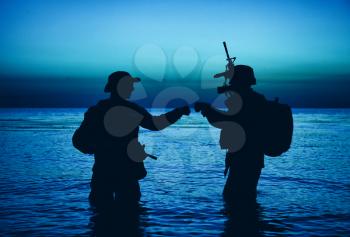 Army special operations forces soldiers, commando fighters doing fist dump gesture while standing knee-deep in water. Two Marines shooters or coast guard fighters celebrating mission successful ending