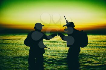 Army special operations forces soldiers, commando fighters doing fist dump gesture while standing knee-deep in water. Two Marines shooters or coast guard fighters celebrating mission successful ending