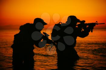 Army soldiers team, special operation forces infantrymen landing on seacoast, aiming and shooting with service rifle during firefight on shore at evening or morning time. Military amphibious operation