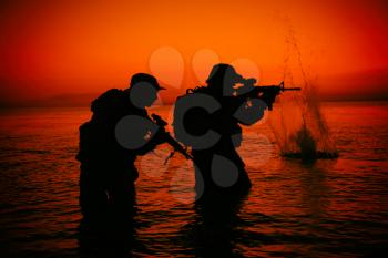 Army soldiers team, special operation forces infantrymen landing on seacoast, aiming and shooting with service rifle during firefight on shore at evening or morning time. Military amphibious operation