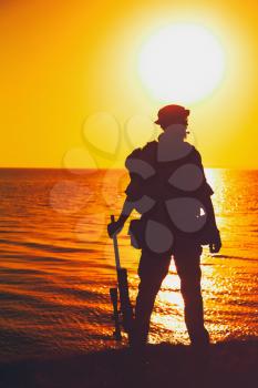 Silhouette of army commando fighter, Navy SEALS team sniper or coast guard soldier standing on sea shore with rifle on background of ocean sunset horizon. Special forces rifleman patrolling coastline