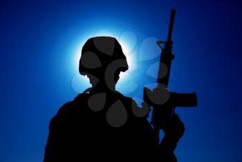 Silhouette of army soldier standing with service rifle in hand on background of night sky with moon. Armed Marines infantry in battle helmet and uniform ready for action, patrolling area in darkness