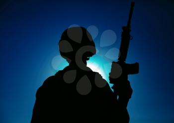 Night silhouette of army special operations forces soldier standing with service rifle on background of night sky with moon and stars. Modern warfare combatant in helmet, Marines raider in darkness
