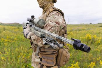 Soldier with sniper rifle standing in blooming green field