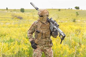 Soldier in a special military uniform, with a helmet on his head and with a sniper rifle in the field
