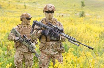 Two armed special forces soldiers with sniper rifles standing in the blooming field