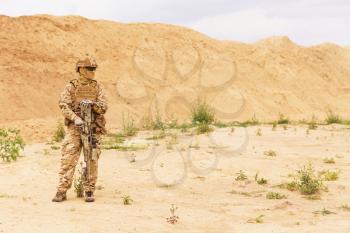 Equipped and armed special forces soldier, army ranger standing in the desert with copy space. Concept of military anti-terrorism operations, special operations of NATO forces.