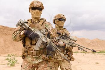 Two equipped and armed special forces soldiers standing in the desert. Concept of military anti-terrorism operations, special operations of NATO forces.