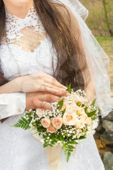 Hands and rings on wedding bouquet.