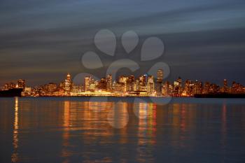 Night city, panoramic scene of downtown reflected in water. Sunset above Vancouver, Canada