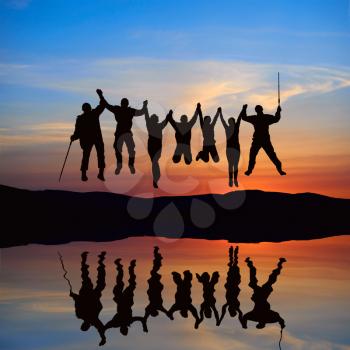 Silhouette of jumping friends on the beach with reflection against sunset