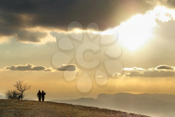 Couple on the hill against sunset. Landscape with clouds and sky.