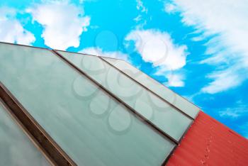 Solar system on the red house roof with blue sunny sky and clouds.