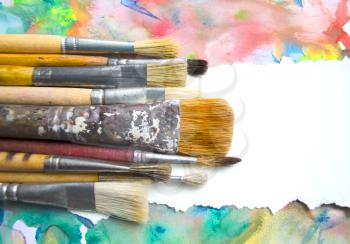 A group of paintbrushes on abstract colorful watercolor background with place for text. Can be used for background, banner, poster, advertising workshops. Blank for motivating quote, note, message.