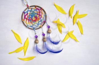 Dreamcatcher with blue feathers between the yellow sunflower petalson an wooden background . Ethnic design, boho style, tribal symbol.