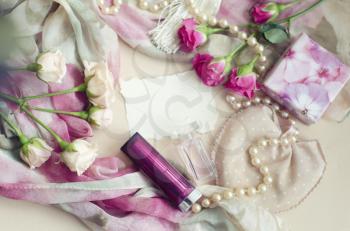 Photocomposition in a gentle vintage style in pastel colors. Tea pink roses lie on a silk scarf, surrounded by pearls, lipstick,perfume. Photo can be as a frame for the message to woman.Place for text