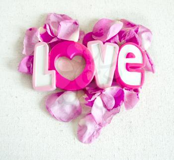 The word Love and rose petals in form of heart isolated on white textile background. Valentines day concept.