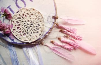 Dreamcatcher with pink feathers and roses on a wooden background. Ethnic design, boho style, tribal symbol.