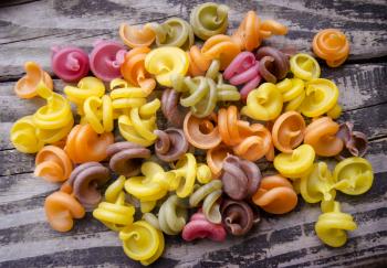 Heap of colored italian pasta on old woden desk. Bunch of raw pasta isolated on gray striped background.