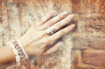 Close-up of female hand with ring and bracelet on a brick wall. Collage in vintage style, image of beautiful female hand with ethnic ornaments on a background of ancient stone wall.