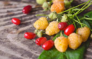 Yellow raspberry and cornel fruits with leafs on old textured wooden background. Organic berries closeup. Ripe fresh white raspberry and dogwood.