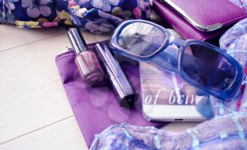 Fashionable female accessories watch sunglasses lipstick violet clutch and mobile phone. Different objects on wooden background. Woman's things.