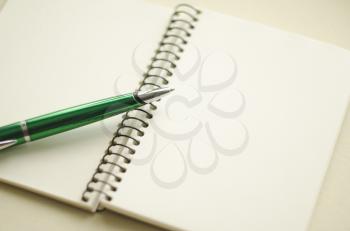 A part of open blank white notebook and green pen on the desk.
