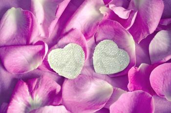 Background texture of beautiful delicate pink rose petals in a random pile and two hearts. The concept of love and romance. Valentines Day decoration.