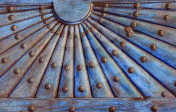 Ornate wooden pattern with metal rivets. Relief wooden part of old door with geometrical ornament in the form of the sun with rays.