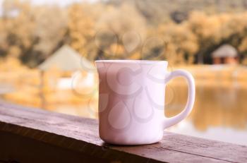 Porcelain white cup on the porch overlooking the lake. Travel autumn photo.