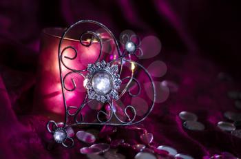 Vintage metal heart with a crystal on a background of violet drapery with lights of the garland. Mysterious Valentine's Day Concept.