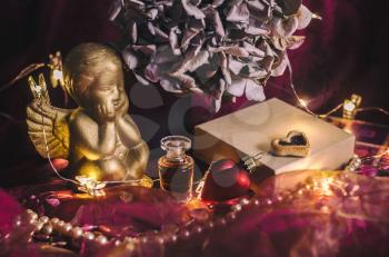 Composition with a golden cupid, gift box, perfume, hydrangea flower in mystical dark lighting. Valentin's day concept