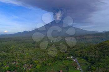 Ashes rising from the volcano. The village at the foot of the volcano in the tropical jungle.