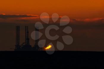 Drilling platform in the port. Oil platform at sunset with a burning torch. Towing of the oil platform.