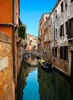 Beautiful view of the bridge over narrow venetian сanal with boats and colorful facades of old medieval houses. Venice, Italy 