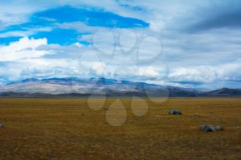 Bright steppe landscape with a piece of rock in the foreground, mountains view, blue sky with clouds. Chuya Steppe,  Kuray steppe in the Siberian Altai Mountains, Russia