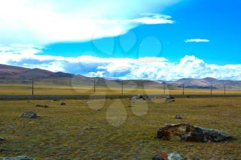 Bright steppe landscape with a road and big piece of rock in the foreground, mountains view, blue sky with clouds. Chuya Steppe,  Kuray steppe in the Siberian Altai Mountains, Russia